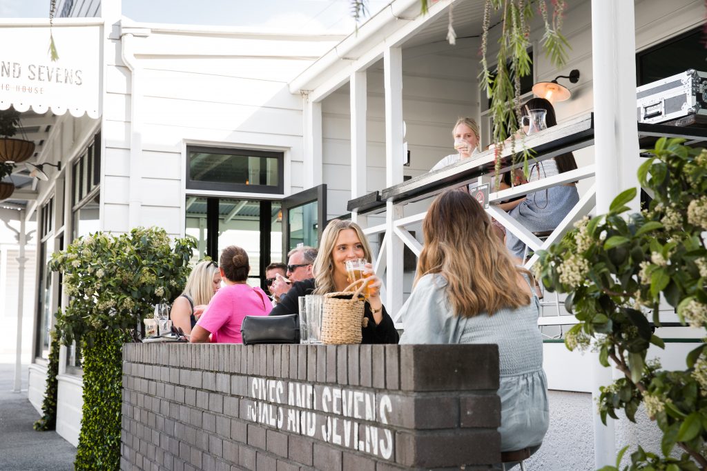 People sitting and drinking outside at a hospitality venue with plants and greenery around